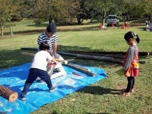 「三木市三木山活動地」が参加した三木山森林公園の森の日イベント「楽木市」での丸太切りに挑戦する兄弟